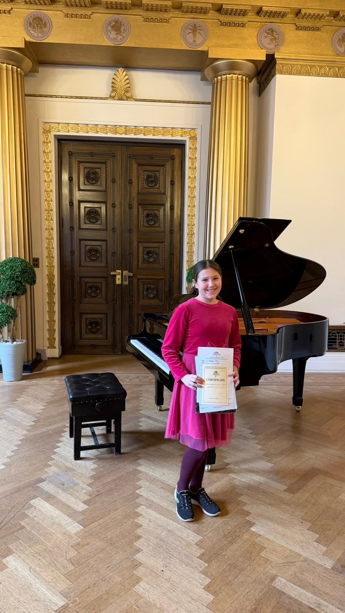 A pianist holding a competition certificate in a grand hall