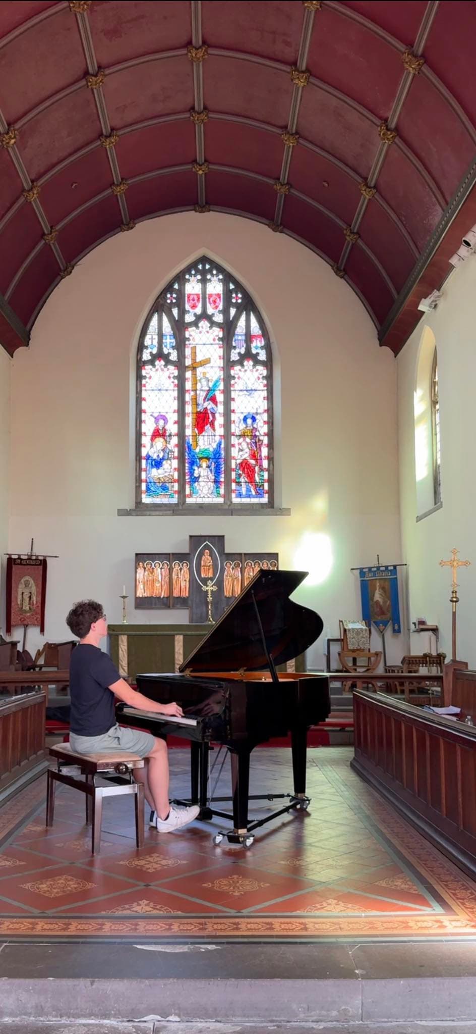 A student at a grand piano beneath a stained-glass window